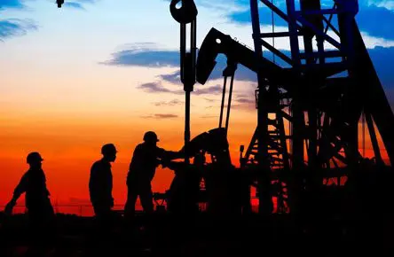 Two men are standing next to a pump jack.